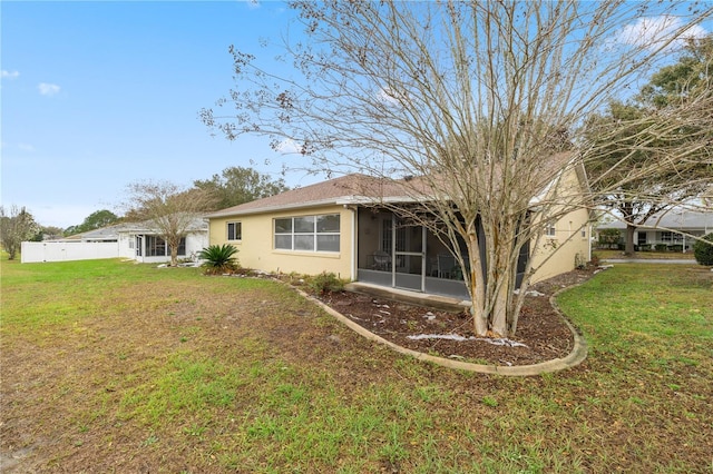 back of house featuring a sunroom, a yard, and stucco siding