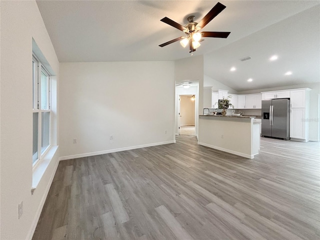 unfurnished living room with light wood finished floors, visible vents, baseboards, ceiling fan, and vaulted ceiling