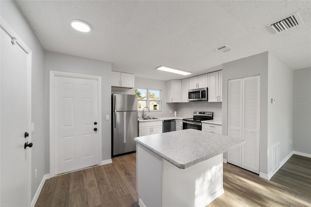 kitchen featuring stainless steel appliances, a sink, visible vents, light countertops, and dark wood finished floors