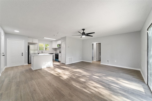 unfurnished living room with baseboards, visible vents, wood finished floors, a textured ceiling, and a sink