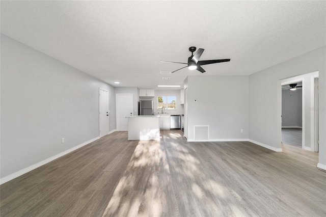 unfurnished living room with visible vents, a textured ceiling, and wood finished floors