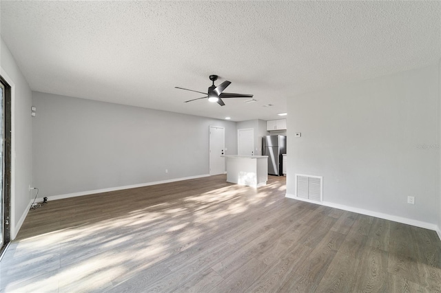 unfurnished living room with visible vents, a ceiling fan, a textured ceiling, wood finished floors, and baseboards