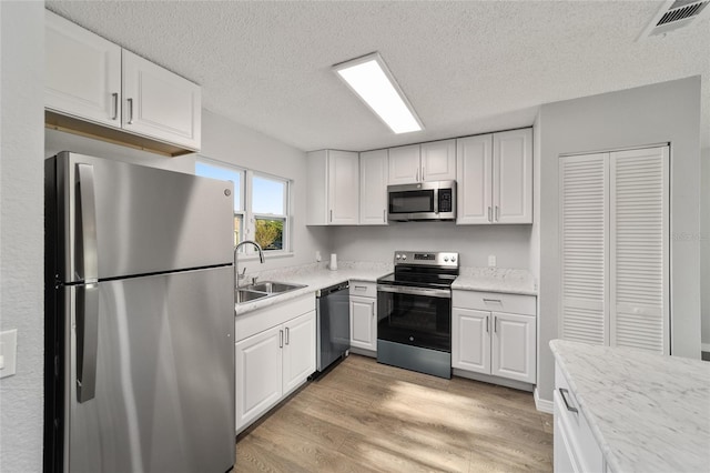 kitchen with appliances with stainless steel finishes, light wood-type flooring, a sink, and white cabinets