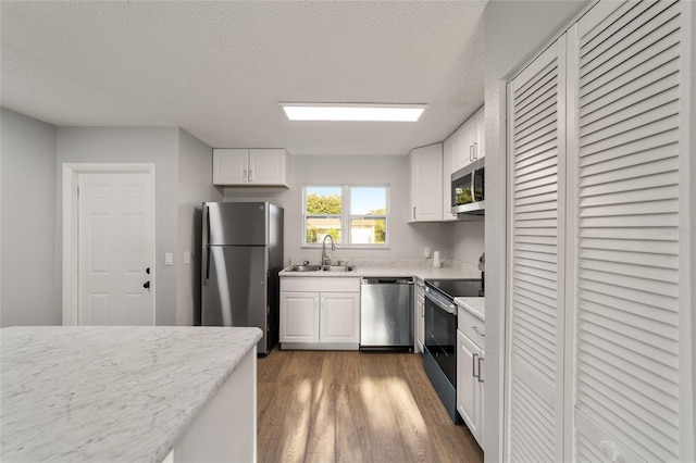 kitchen with appliances with stainless steel finishes, dark wood-style flooring, white cabinetry, and a sink