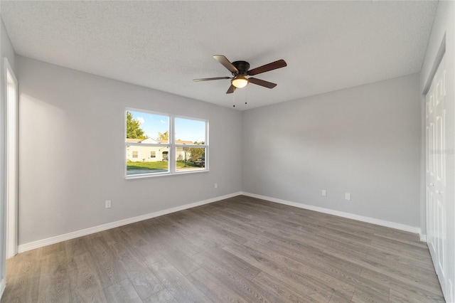 empty room with a textured ceiling, wood finished floors, a ceiling fan, and baseboards