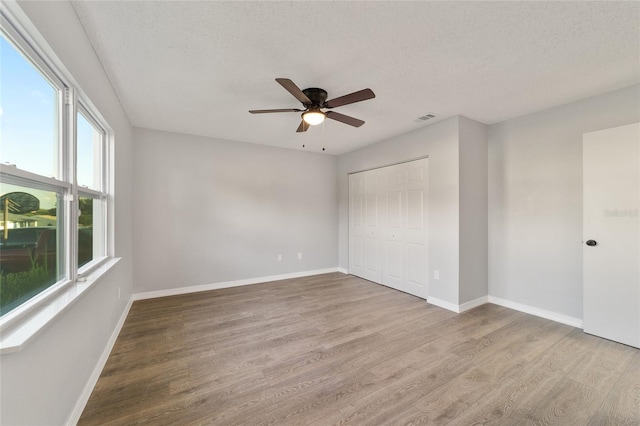 unfurnished bedroom featuring a closet, visible vents, a textured ceiling, wood finished floors, and baseboards