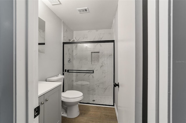 bathroom featuring toilet, visible vents, wood finished floors, and a marble finish shower