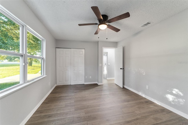 unfurnished bedroom with visible vents, a textured ceiling, baseboards, and wood finished floors