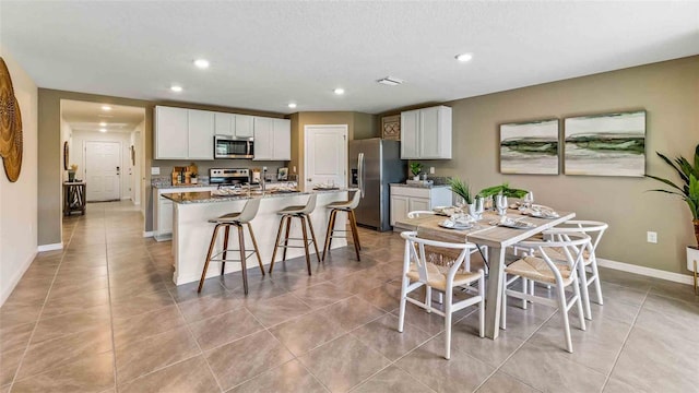 kitchen with a breakfast bar area, appliances with stainless steel finishes, stone countertops, white cabinets, and a kitchen island with sink