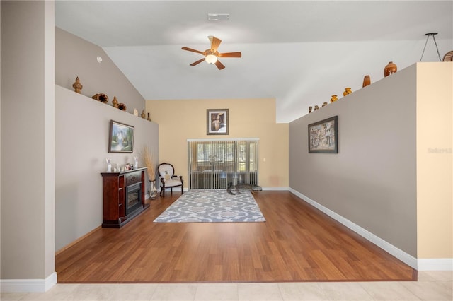 interior space with lofted ceiling, wood finished floors, a ceiling fan, baseboards, and a glass covered fireplace