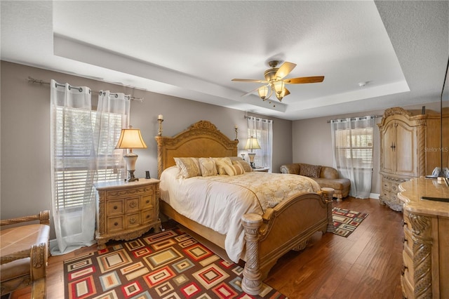 bedroom with a tray ceiling, ceiling fan, a textured ceiling, wood finished floors, and baseboards