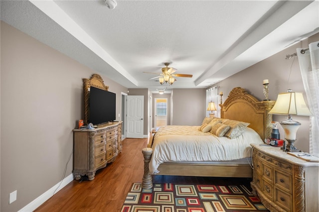 bedroom featuring a tray ceiling, a ceiling fan, a textured ceiling, wood finished floors, and baseboards