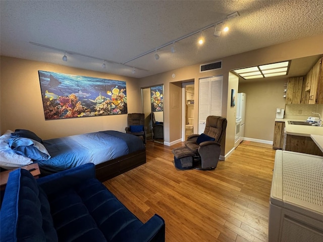 bedroom with a textured ceiling, light wood finished floors, visible vents, and baseboards