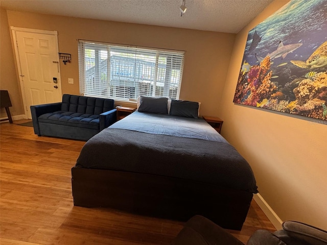 bedroom featuring a textured ceiling, wood finished floors, and baseboards