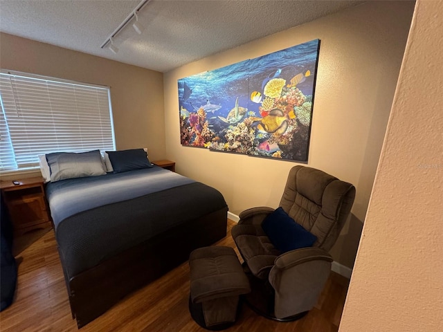 bedroom with a textured ceiling, baseboards, wood finished floors, and track lighting