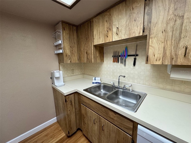 kitchen featuring baseboards, backsplash, a sink, and light countertops