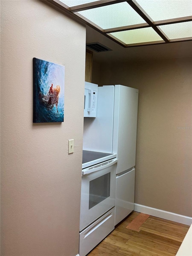 kitchen with white appliances, wood finished floors, visible vents, and baseboards