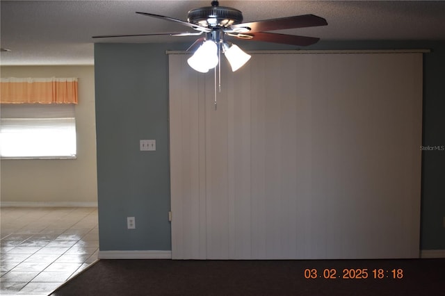 spare room featuring ceiling fan, tile patterned floors, baseboards, and a textured ceiling