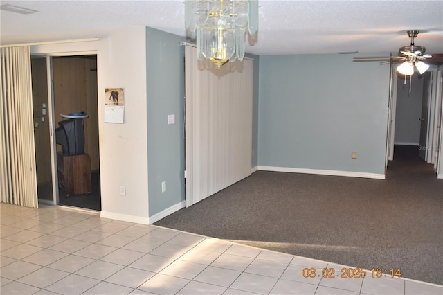 unfurnished room with ceiling fan with notable chandelier, a textured ceiling, carpet floors, tile patterned flooring, and baseboards