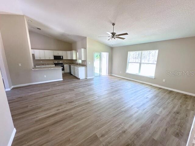 unfurnished living room with lofted ceiling, a textured ceiling, wood finished floors, and a ceiling fan