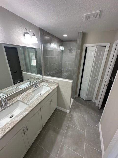 full bathroom with double vanity, a walk in shower, visible vents, and a sink