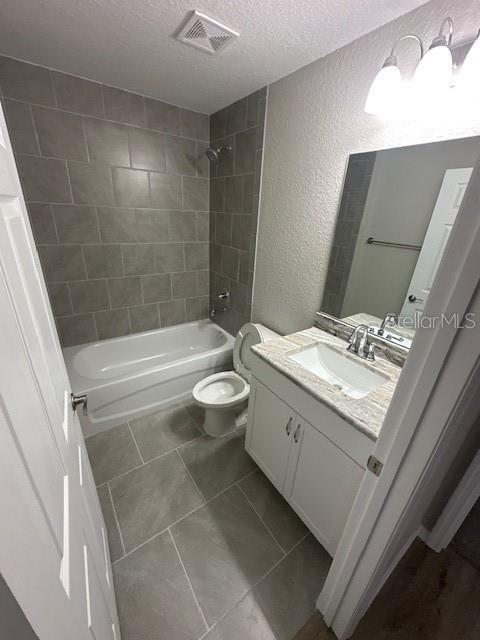 bathroom with visible vents, a textured ceiling, toilet, a textured wall, and shower / bathtub combination