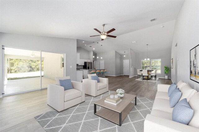 living room with visible vents, baseboards, ceiling fan with notable chandelier, light wood-style floors, and high vaulted ceiling