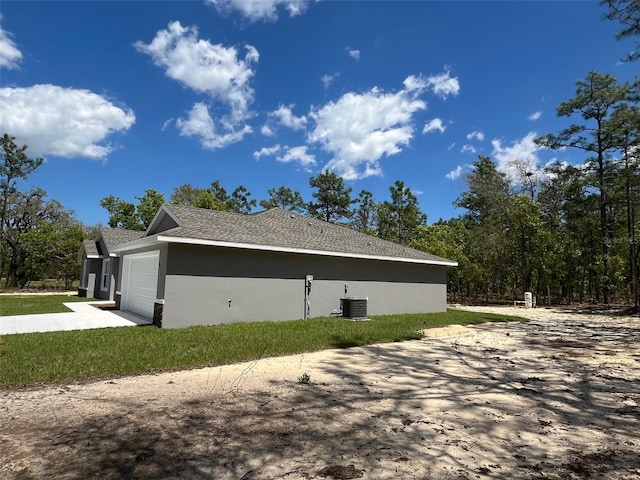 view of side of property with concrete driveway, central AC, stucco siding, a yard, and an attached garage