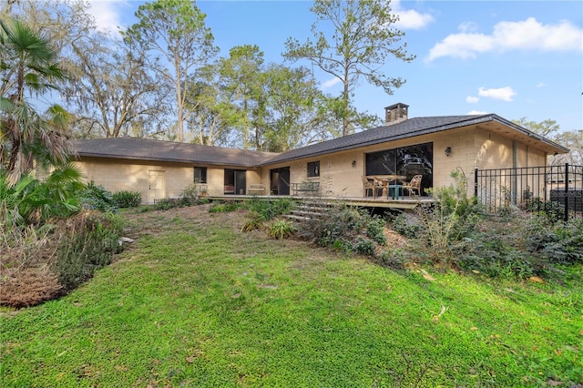 rear view of property featuring a chimney, a lawn, and a deck