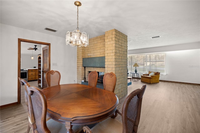 dining space with a brick fireplace, visible vents, and wood finished floors