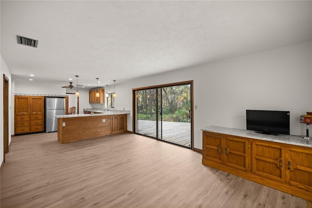 kitchen with visible vents, brown cabinetry, freestanding refrigerator, a peninsula, and light wood-type flooring