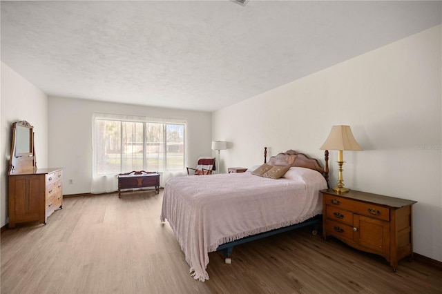 bedroom with light wood finished floors, baseboards, and a textured ceiling