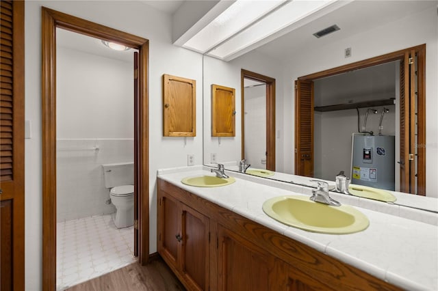 bathroom with toilet, double vanity, a sink, and electric water heater