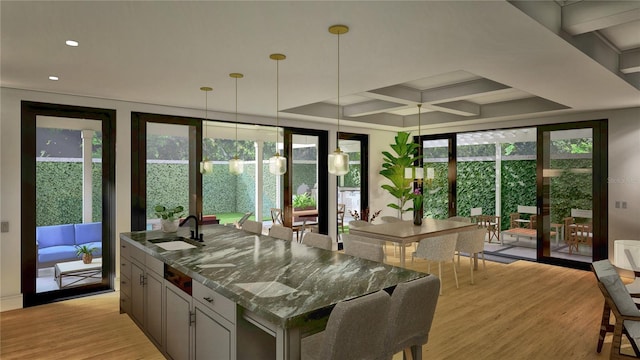 kitchen featuring light wood finished floors, a sink, dark stone countertops, an island with sink, and coffered ceiling