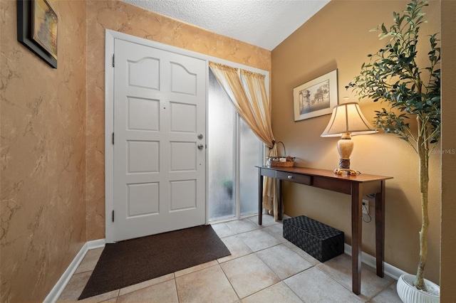 foyer entrance with light tile patterned flooring, a textured ceiling, and baseboards