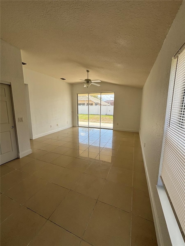 tiled empty room with baseboards, a textured ceiling, a ceiling fan, and vaulted ceiling