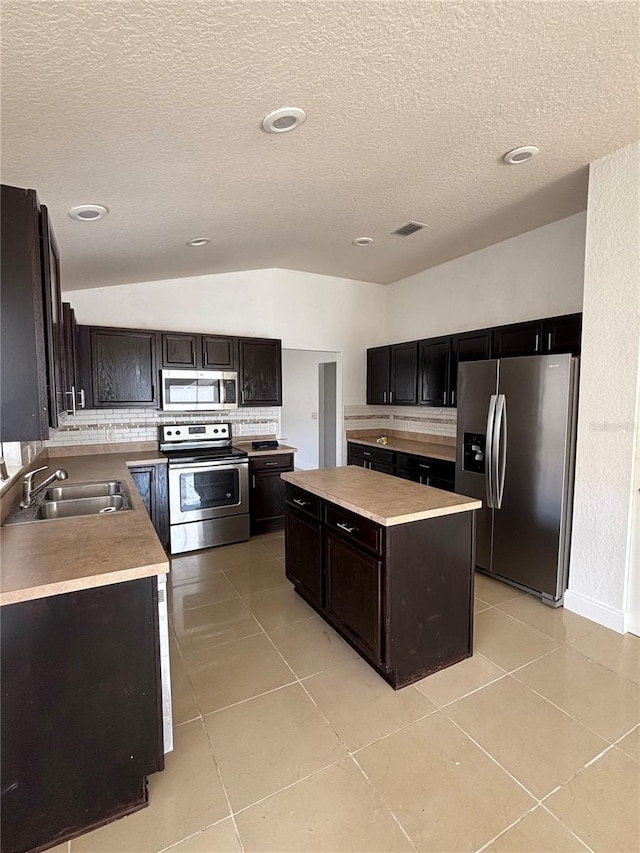 kitchen with light tile patterned flooring, appliances with stainless steel finishes, a kitchen island, and lofted ceiling