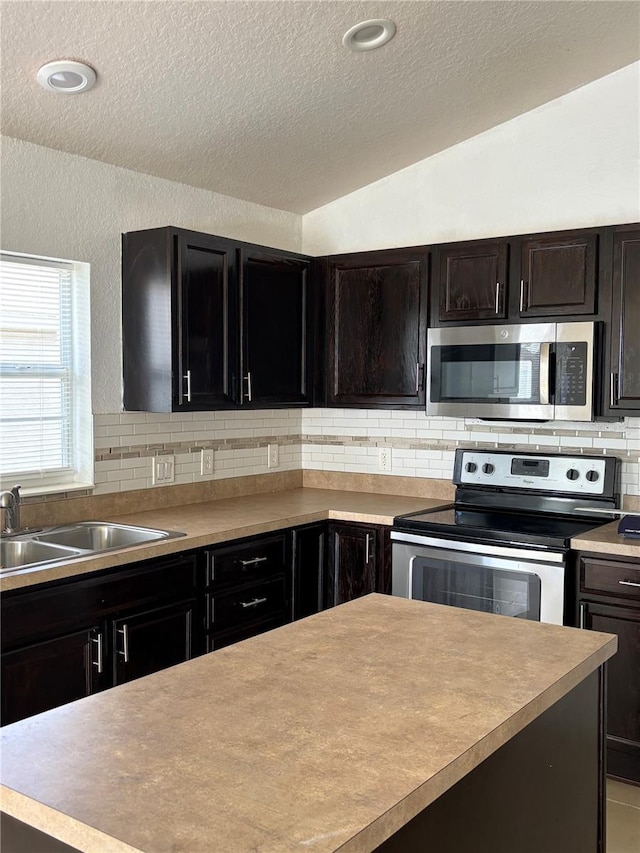 kitchen with lofted ceiling, a sink, light countertops, appliances with stainless steel finishes, and tasteful backsplash