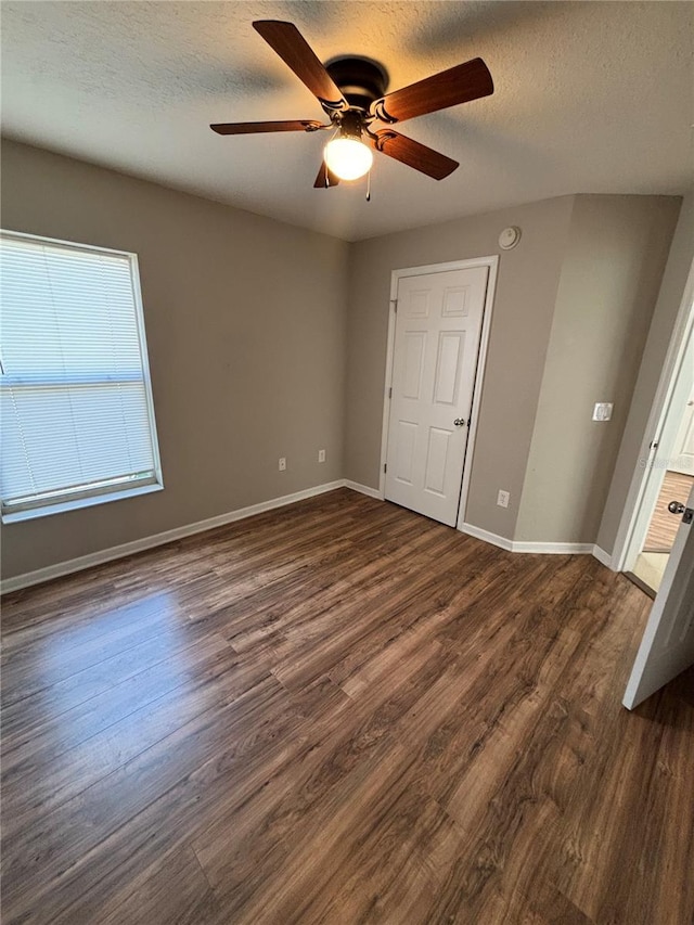 unfurnished bedroom with a textured ceiling, a ceiling fan, baseboards, and dark wood-style flooring