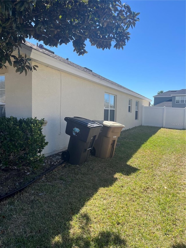 rear view of property with a yard, fence, and stucco siding