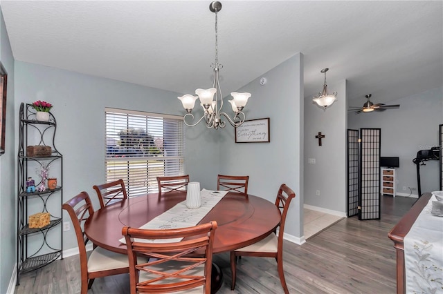 dining area featuring ceiling fan with notable chandelier, lofted ceiling, baseboards, and wood finished floors