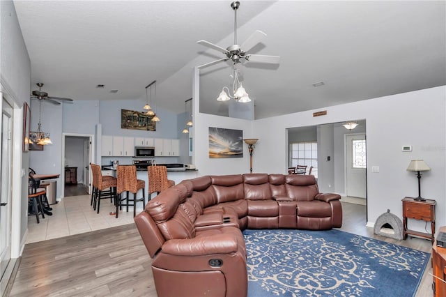 living area featuring ceiling fan with notable chandelier, lofted ceiling, and light wood-style floors