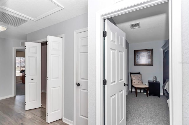 hallway featuring attic access, visible vents, and wood finished floors