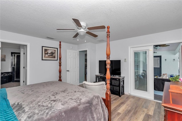 bedroom featuring ceiling fan, a textured ceiling, visible vents, and wood finished floors