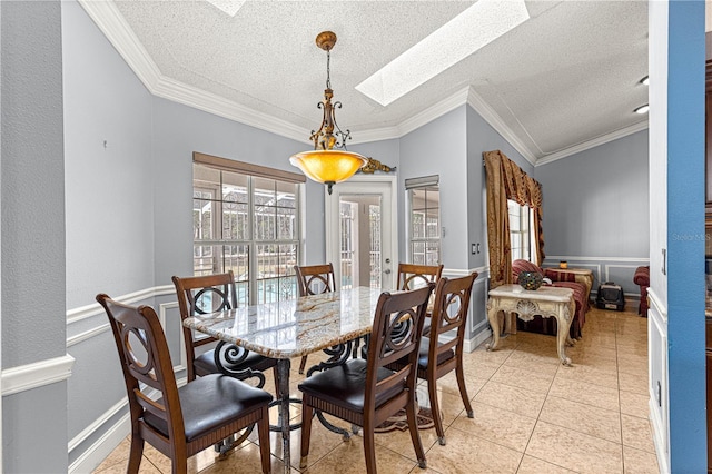 dining area with a skylight, a wainscoted wall, ornamental molding, a textured ceiling, and light tile patterned flooring