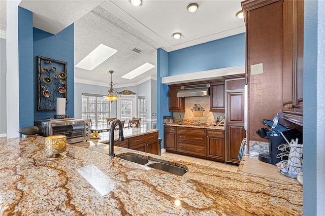 kitchen with a skylight, light stone counters, ornamental molding, extractor fan, and a sink