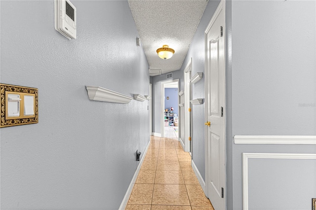 hall with visible vents, baseboards, a textured wall, a textured ceiling, and light tile patterned flooring