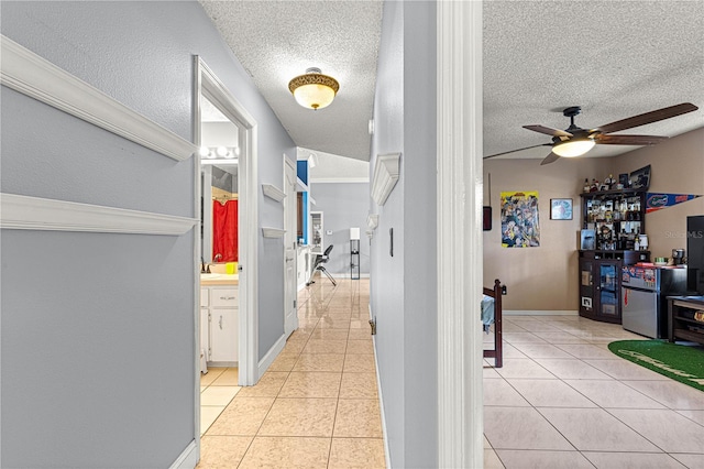 hall with a sink, light tile patterned floors, baseboards, and a textured ceiling