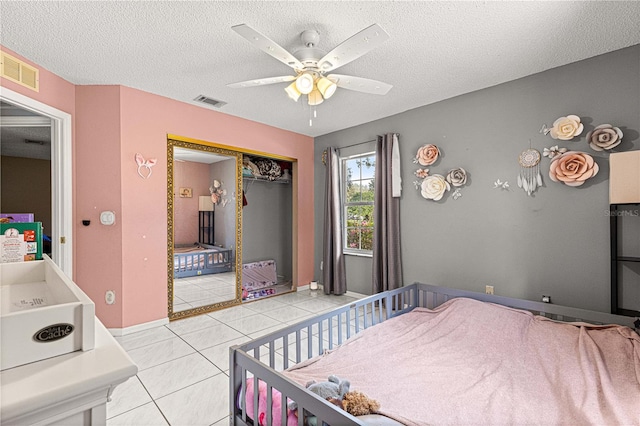 bedroom featuring a closet, visible vents, a textured ceiling, and light tile patterned floors