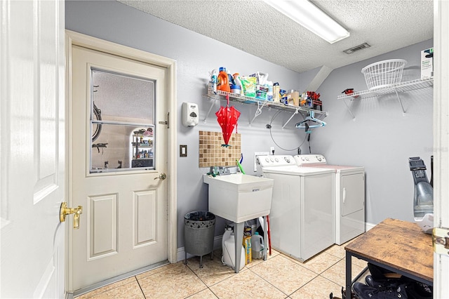 washroom with light tile patterned floors, visible vents, washing machine and dryer, a textured ceiling, and laundry area